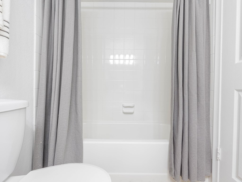 A white bathroom with a white tub and grey curtains.